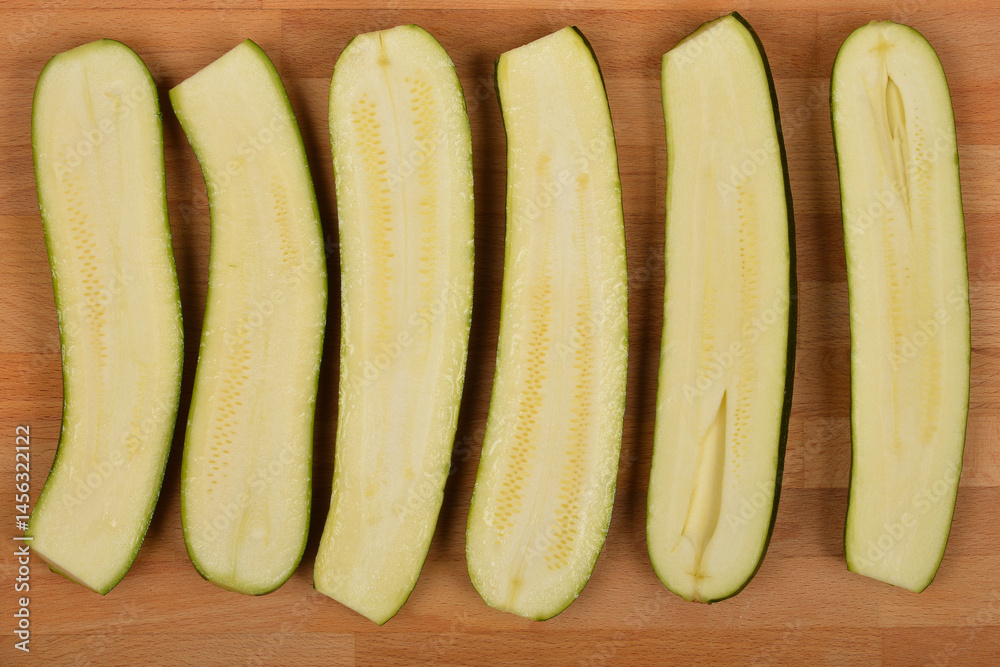 Six halved zucchinis are arranged lengthwise on a light brown wooden surface.