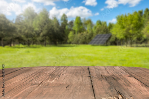 Fototapeta Naklejka Na Ścianę i Meble -  Empty wooden podium with copy space for showcasing eco-friendly or sustainable products and solar panels on lush green field background. Renewable energy and environmental protection concept.