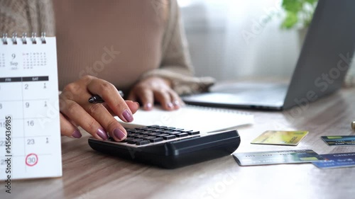financial planning concept with woman hand calculating monthly costs, noting down debts, credit card payments, and upcoming due dates on a calendar