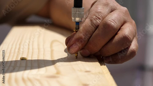 Man aligns two wood pieces, then uses a power drill to insert a long screw into the wooden frame. Detail on the drilling process.