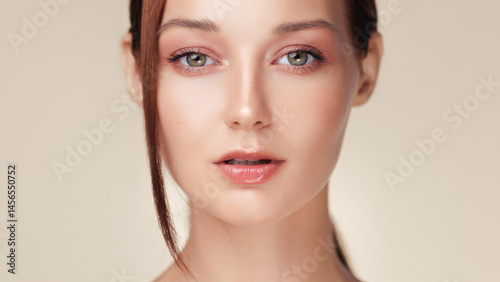 Obraz na płótnie Young woman with glowing skin and peach toned makeup in a close-up studio shot. Great for beauty industry ads, skincare products, or cosmetic promotional banners and editorial content. w salonie