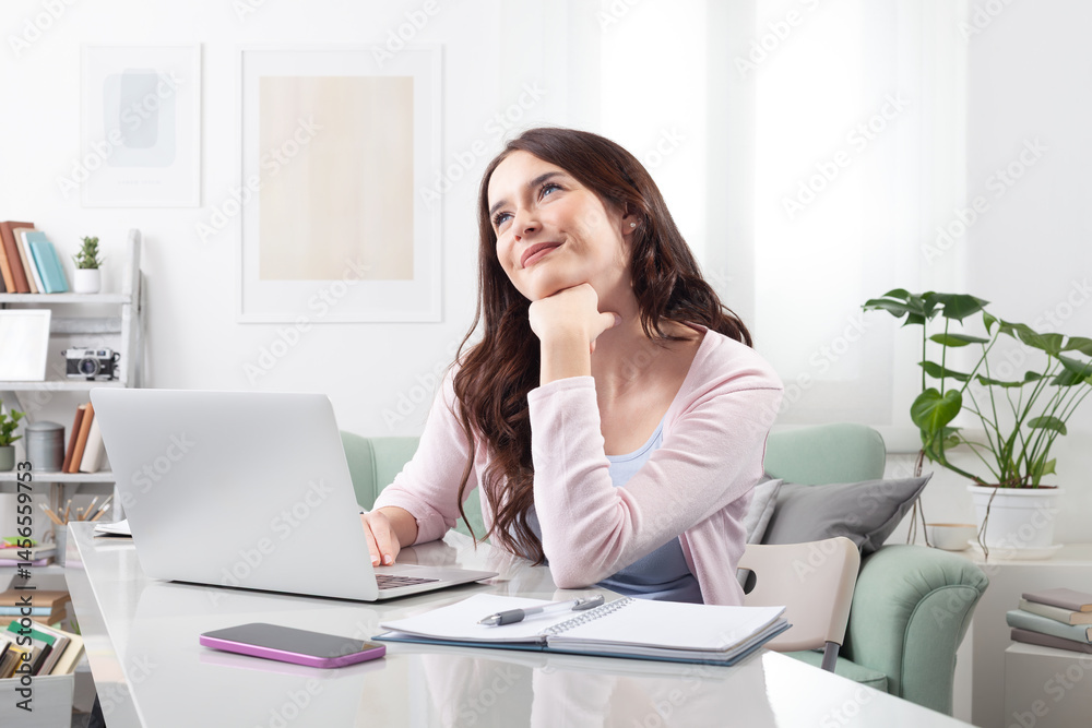 Happy young woman at home, sitting at a desk, using her laptop and daydreaming. Concept of positive remote work, online learning, or college studying with a joyful mindset Happy young woman at home, sitting at a desk, using her laptop and daydreaming. Concept of positive remote work, online learning, or college studying with a joyful mindset