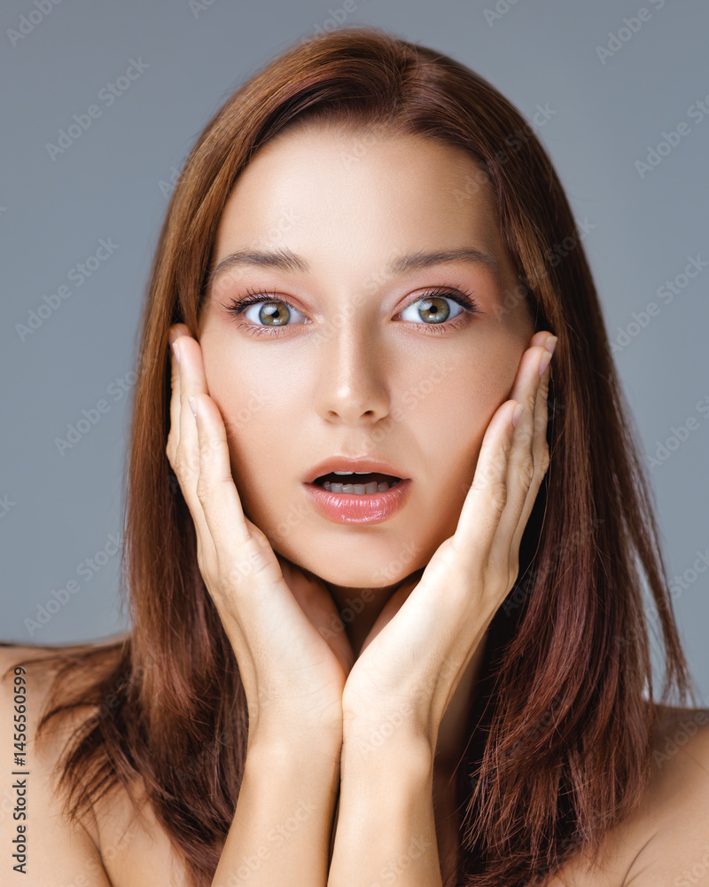 Emotional close-up of a young woman with flawless skin and wide-eyed surprise, hands touching face - perfect for beauty, skincare ads, and expressive lifestyle visuals.