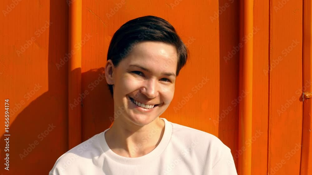 Woman smiling brightly against orange background: joyful expressions and natural sunlight Woman smiling brightly against orange background: joyful expressions and natural sunlight
