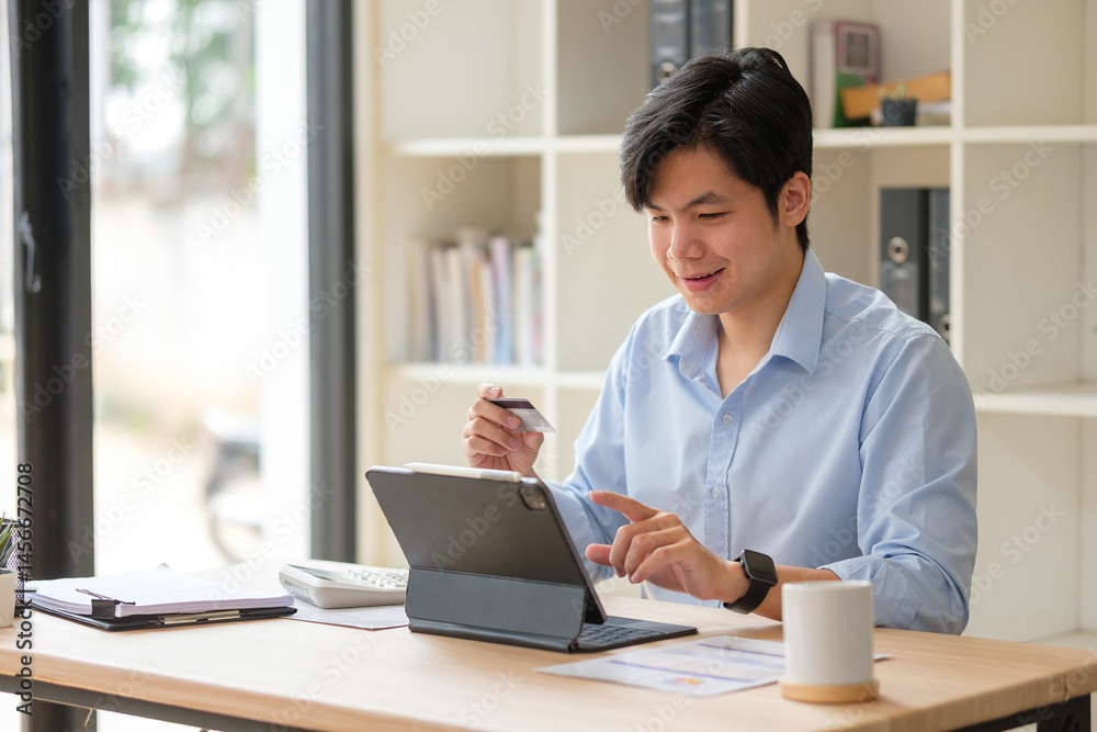 Smiling businessman holding a credit card and using digital tablet, making online purchase at his desk in an office. Smiling businessman holding a credit card and using digital tablet, making online purchase at his desk in an office.