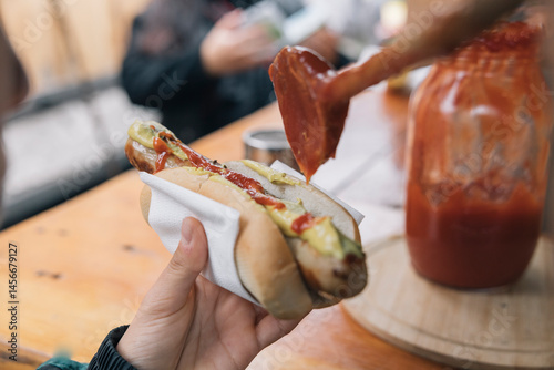 Bratwurst being topped with mustard and ketchup at a street food stall