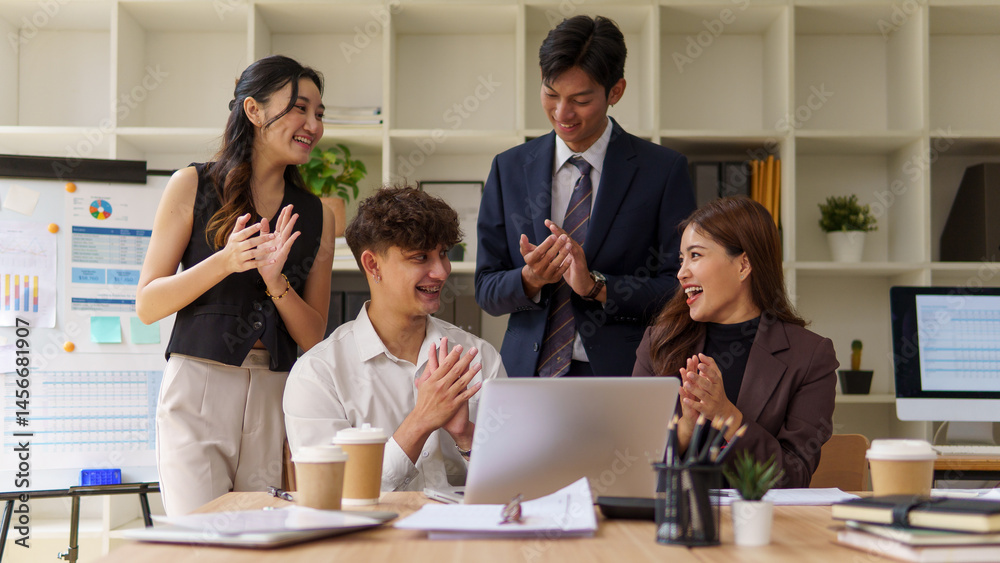 Fototapeta premium Group of happy business people clapping and smiling while looking at a laptop during a successful team meeting.