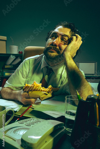 Obraz na płótnie Daydreaming office worker holding sandwich, looks up with bored face at cluttered desk, showing fatigue, absurdity, nostalgia, pressure and corporate burnout. Concept of retro office , overwork w salonie