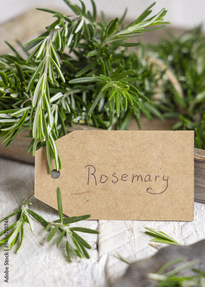 Kraft paper text label near fresh green rosemary sprigs in a basket on white rustic table closeup