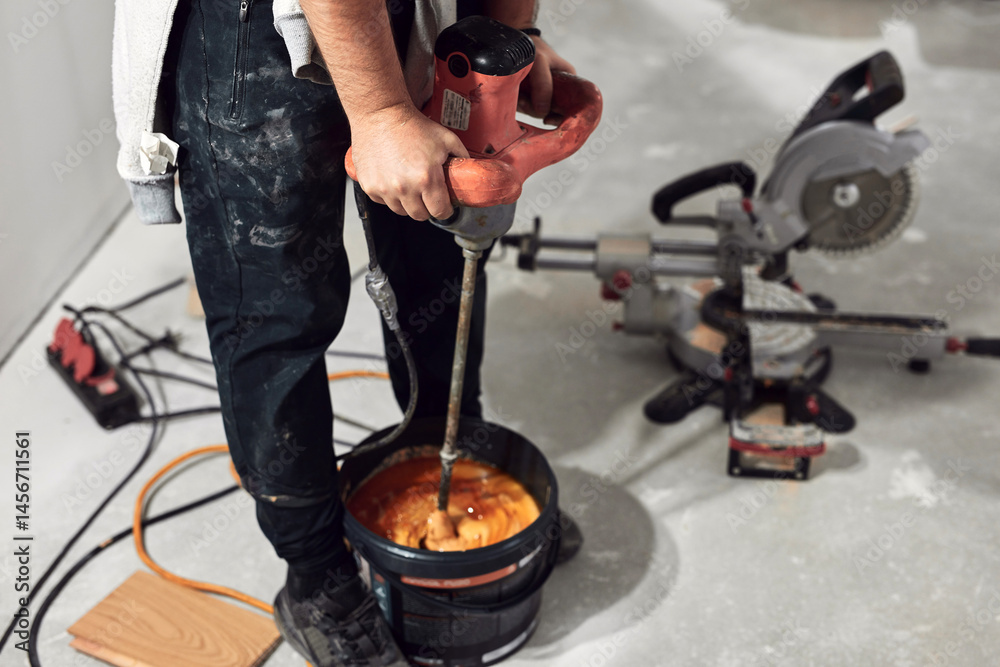 Workers with industrial mixer on a construction site and a bucket of parquet glue.