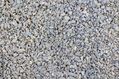 Close-up view of a uniform layer of gray crushed gravel stones, ideal for construction, road base, landscaping, or texture background. Natural rough texture with hard angular edges. High quality photo