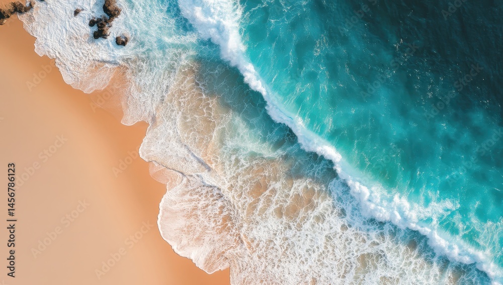 Aerial view of turquoise waves gently washing onto a sandy beach with scattered rocks.
