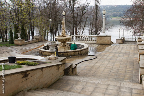 Worker cleaning an old stone fountain in a park during early spring day.
