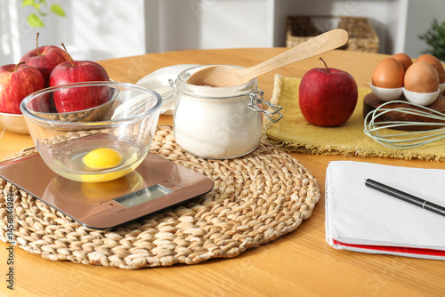 Electronic kitchen scale, products and stationery on wooden table indoors