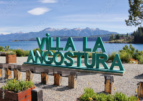 Sign reading Villa La Angostura on the shore of a lake indicating this location in Patagonia