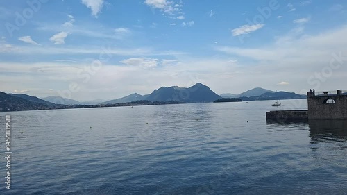 Lake Maggiore, Arona, Italy - May 3 2025: Mountains reflect in calm lake waters at twilight, as the lakeside town of Arona settles into a tranquil summer evening hush.