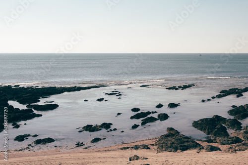 A peaceful rocky beach with calm ocean waves gently washing over the shore under a clear sky.
