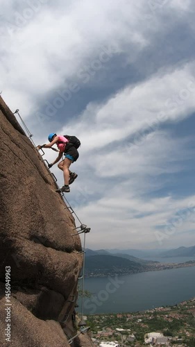 Via Ferrata Picasass, Baveno, Lake Maggiore - Midway through the move, the climber steps onto an exposed overhang, legs extended toward holds anchored in metal pieces above the bay of Lake Maggiore.