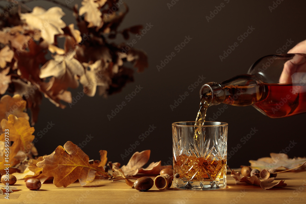 Obraz premium Whiskey with ice on a wooden table with dried-up oak leaves.