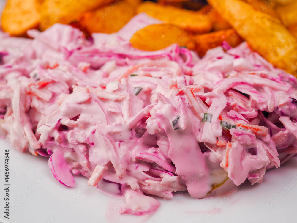 Simple meal with pork belly, potato wedges and pink coleslaw on white plate. Fine dinner with simple products.