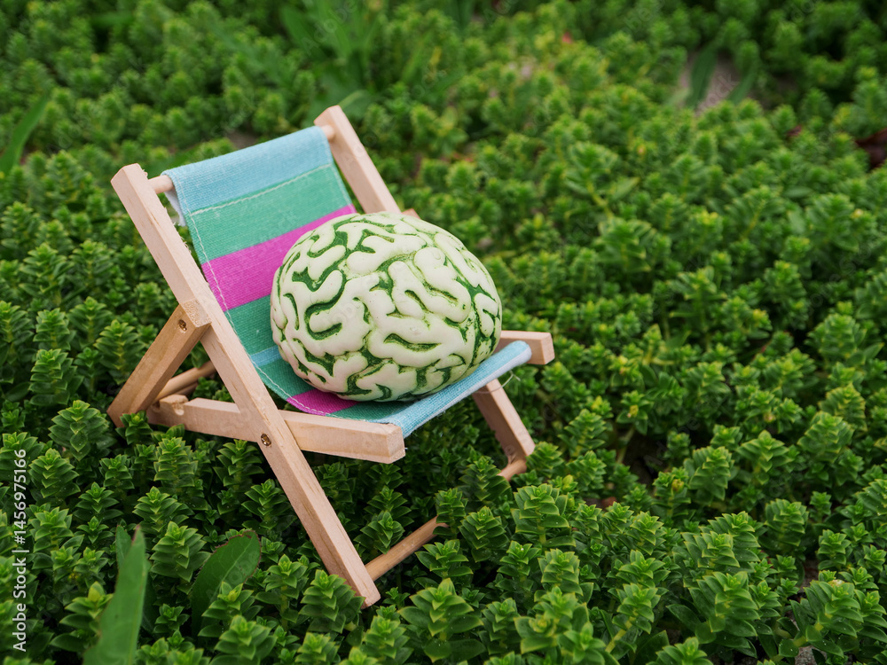 A brain is on a sun lounger bed in a calm nature environment. Relaxation of mind concept with help of fresh air and beautiful scenery. Time for a break theme. Avoid burn out measure