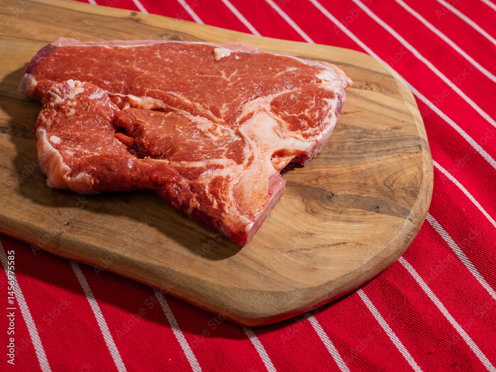 Fresh uncooked T bone steak on a wooden cutting board and on classic red and white stripe table cloth. High quality beef meat product. Butcher craft.