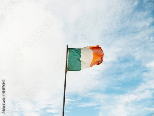 Obraz na płótnie Irish national flag waving on a pole, blue cloudy sky background. w salonie