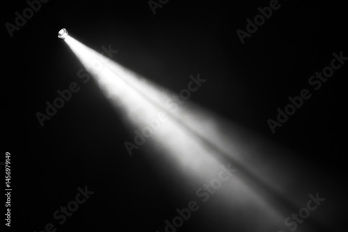 A single spotlight shines brightly through a hazy, dark, and atmospheric space creating a stark contrast.