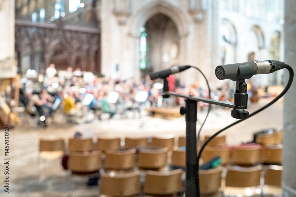 Shallow focus of a professional singers microphone seen near a classical orchestra in rehearsal for a forthcoming public event. A large number of seats can be seen, which will be used by the public.