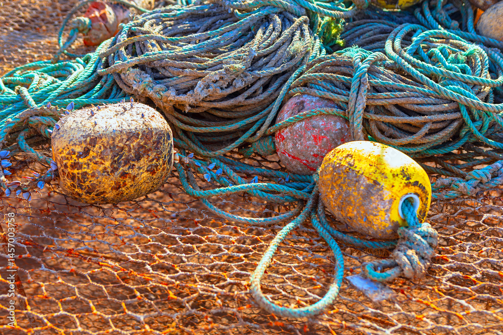 Tangled pile of weathered fishing ropes and nets, accompanied by worn, buoys in shades of yellow and brown. Scene captures rugged, hardworking essence of maritime life, with equipment spread out