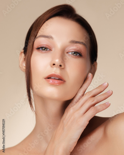 Obraz na płótnie Closeup beauty portrait of a young Caucasian woman with glowing skin and glossy lips softly touching her face, ideal for skincare, anti-aging products, or high-end cosmetic campaigns. w salonie