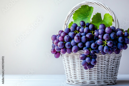 Obraz na płótnie Freshly Harvested Purple Grapes in a Decorative Basket on a Light Surface Surrounded by Green Leaves w salonie
