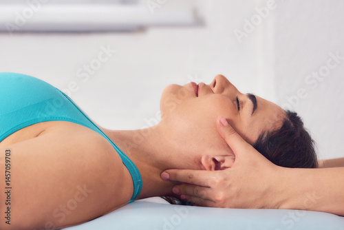 Gentle craniosacral therapy performed by an osteopath, targeting neck pain on young beautiful woman in blue top. Close up   