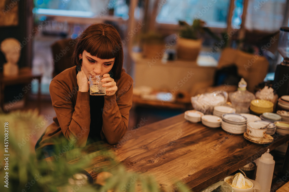 A woman sitting alone at a wooden table, holding a glass, looks thoughtful and introspective. The cozy interior adds a warm atmosphere, contrasting with her contemplative mood.