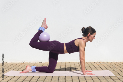 Tableau sur toile Toned woman doing pilates exercise, donkey kick with ball