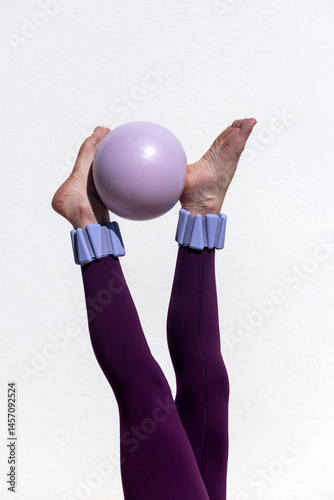 Close up of a fit woman doing pilates exercises with a ball, legs raised with adjustable ankle weights