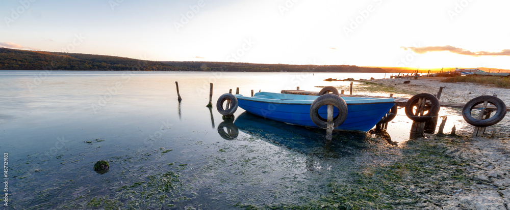 beauty sunset with the lonely blue boat on the beach
