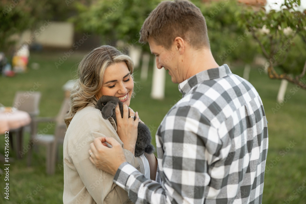 Fototapeta premium A couple shares a warm moment with their pet bunny while enjoying a serene outdoor setting filled with greenery.
