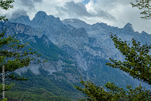 Mountains rise behind trees under a cloudy sky: Accursed Mountains, Albanian Alps, Albania