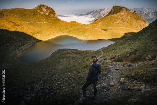 Female hiker admiring the breathtaking view of lac de montagnon in the pyrenees mountains at sunrise