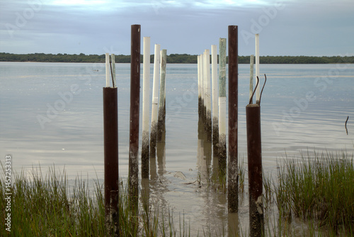 Posts standing on the shore of Cananeia channel early morning at sunrise. Calm waters, clear sky, sunny day
