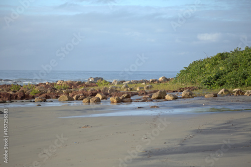 Itacuruca beach, Cananeia, south Sao Paulo state, rocks spread out on beach sand, green vegtaion, clear blue sky, sunny day morning