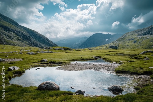 Mountain valley with a placid pond reflecting the sky.  A grassy meadow nestled between steep slopes, bathed in sunlight, under a partly cloudy sky
