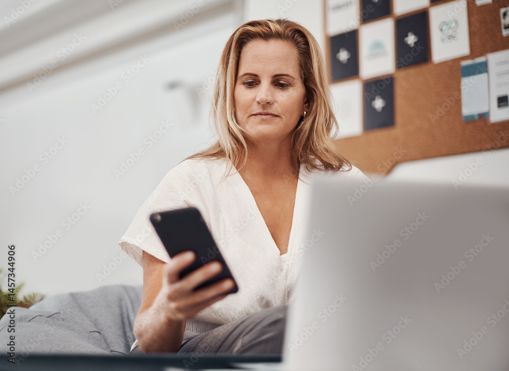 Smartphone, business woman and reading email, social media or notification on laptop in startup. Mobile, typing and professional scroll online for article, blog or creative copywriter research info