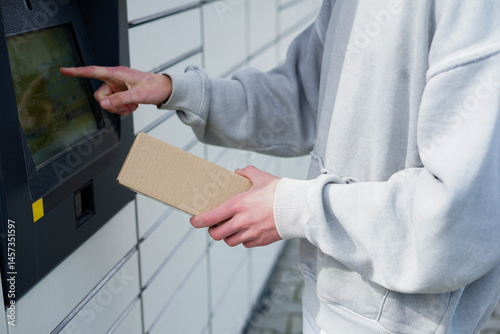 Man placing parcel into outdoor self-service locker touchscreen. Young man uses touchscreen to pick up a cardboard package from a self-service parcel locker