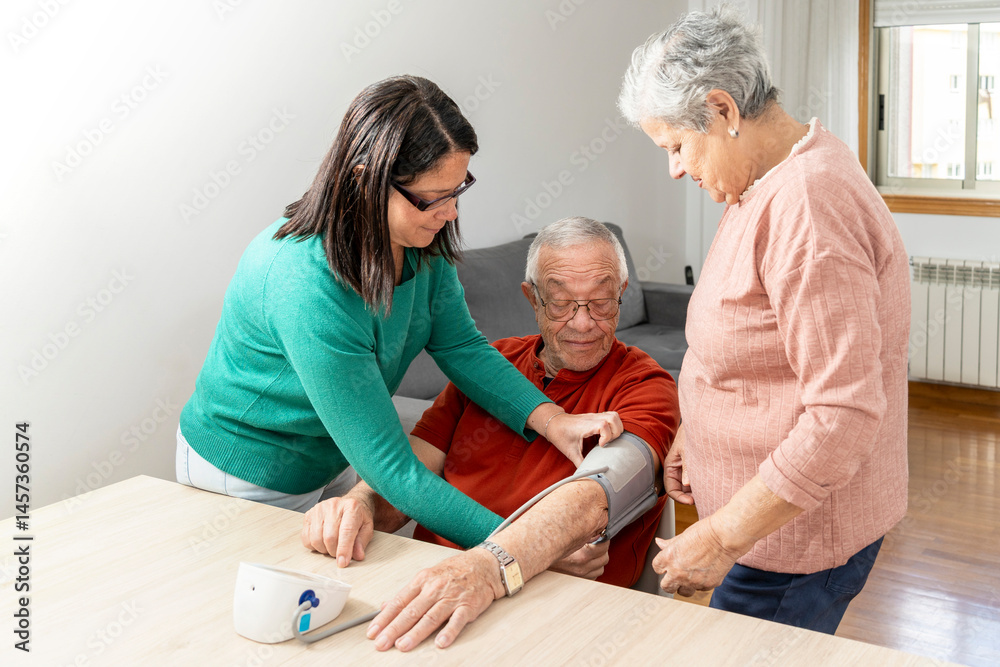 Fototapeta premium Daughter and wife taking blood pressure of smiling senior man with tensiometer at home