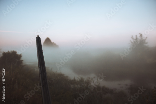Hunting shotgun barrel aiming during foggy morning on river bank during hunting season as hunting background in old vintage style 