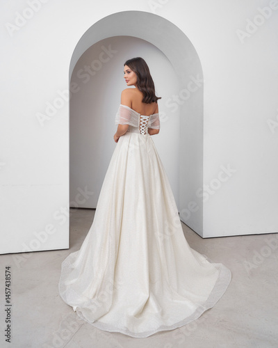 Brunette woman in wedding dress poses gracefully in bright interior with arch