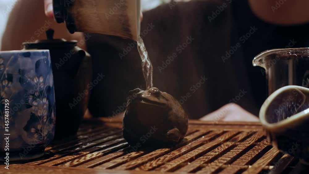 Close-up of a tea master pouring hot water from a clay teapot and cup onto a small clay frog, a symbolic gesture in Chinese tea culture.