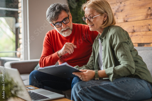 Foto aged woman and man work from home while use clipboard and laptop